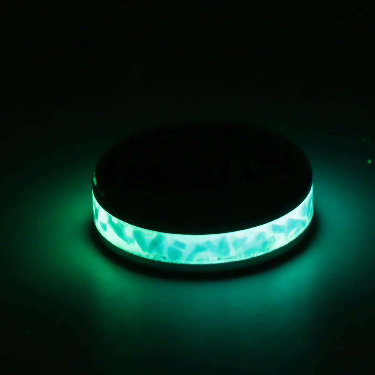 Round glowing ring with a black band and greenish-blue inlay on a dark background