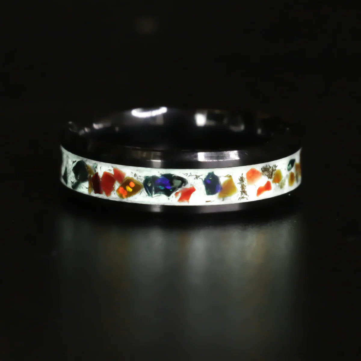 Black ring with colorful opal inlay with white glow powder design on a dark background