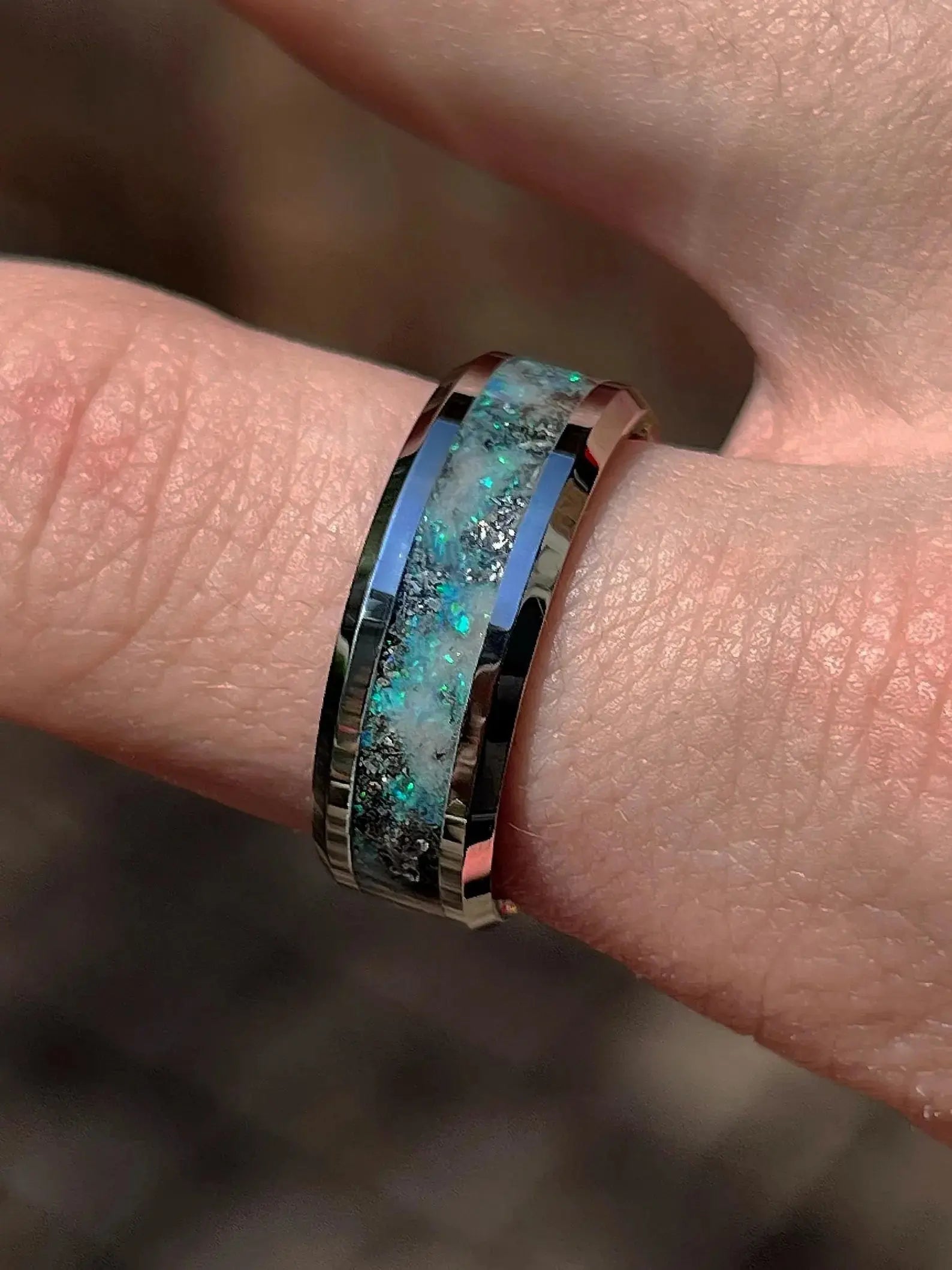 Ring with a blue and green gemstone on a finger against a blurred background